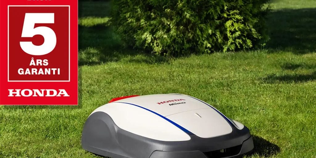A robotic mower on green grass, featuring a warranty sign.