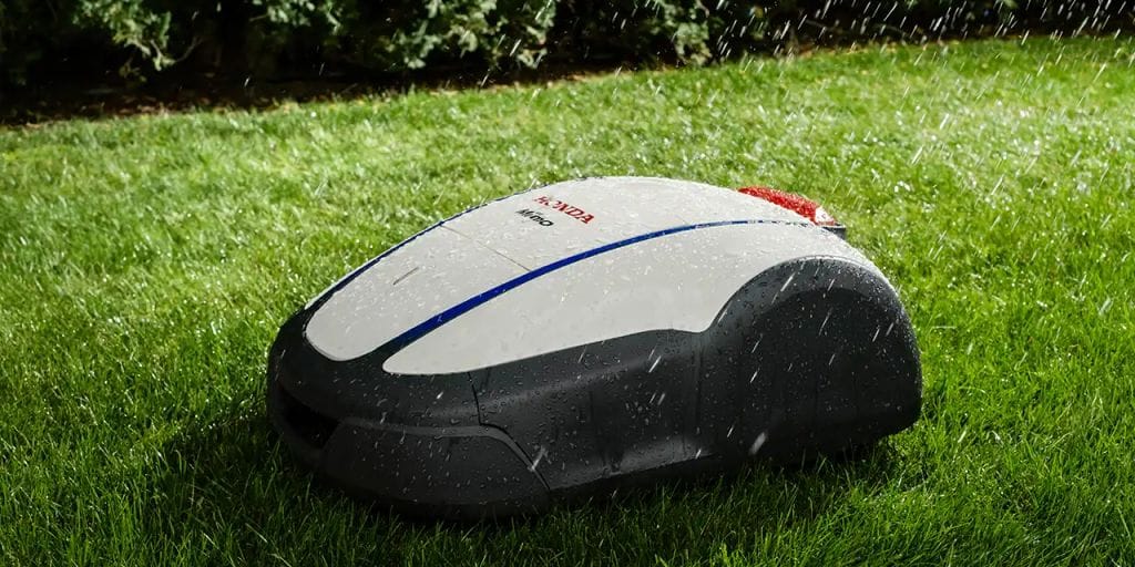 A robotic lawn mower on wet grass in a garden.